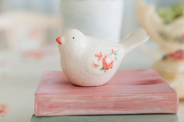 istock Delicate ceramic bird figurine perched on pastel-colored books, surrounded by floral decorations and an ornate vase. The soft lighting and gentle colors evoke a sense of tranquility and charm 2156804328