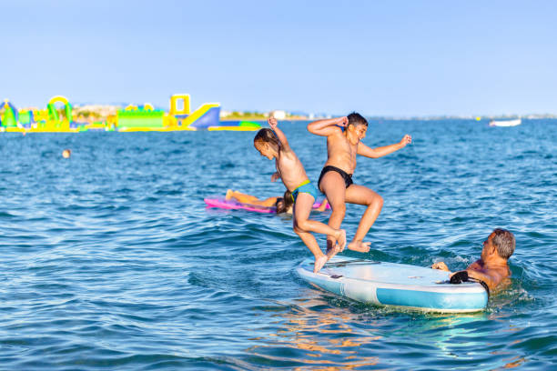 istock Caucasian brothers with father playing in the sea while jumping from a standup paddleboard 2156810183