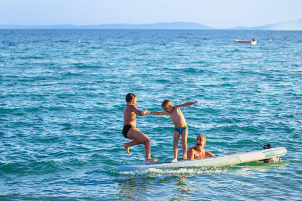 istock Sons with father playing in the sea while jumping from a standup paddleboard 2156814487