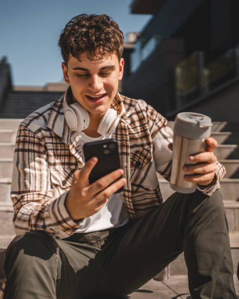 istock Young boy with headphones and thermos cup sit and use mobile phone 2156817849