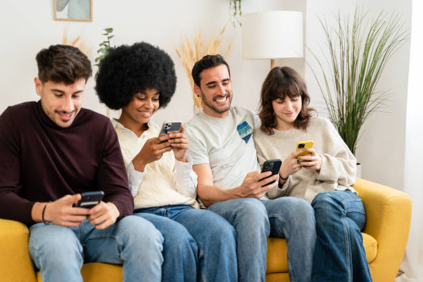 istock Four friends sit together on a yellow couch, each using their smartphone 2156818052