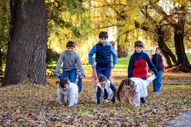 Happy children playing wheelbarrow race outside and mother supporting on background- Buenos Aires - Argentina