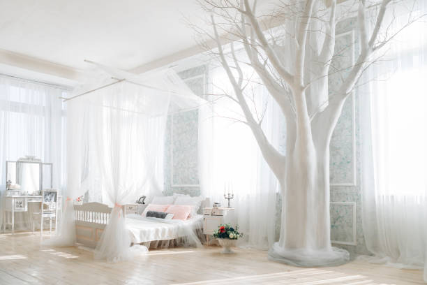 istock Ethereal bedroom with white canopy bed, pastel pillows, ornate vanity, large white tree decor, floral bouquet, sunlight streaming through sheer curtains, airy and tranquil ambiance 2156822192