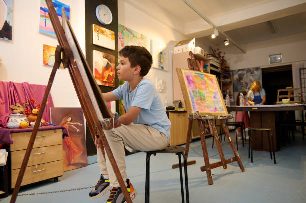 istock Young boy drawing and painting in art class with teacher in creative workshop 2156826543