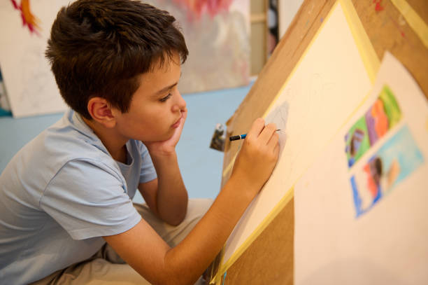 istock Boy concentrating on drawing during art class workshop with colorful paintings 2156829327