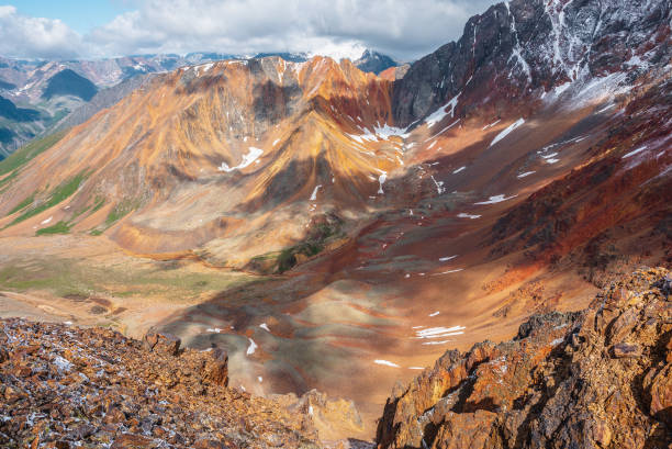 istock Top view from rock abyss edge to rounded multicolor valley with curved iron river and big sharp rocky ridge of red color. Colorful large mountains. Rocks in freshly fallen snow. Vivid alpine scenery. 2156838154