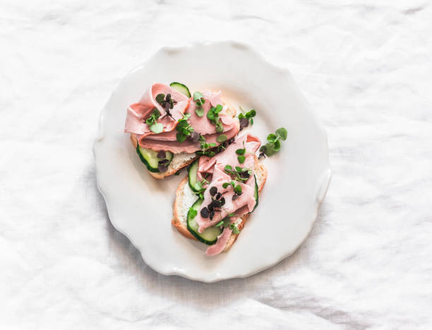 Delicious breakfast, snack, tapas - sandwiches with ham, cucumber and microgreens on a light background, top view
