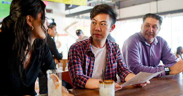 istock Three Patrons at a Bar Counter Have a Conversation While One Holds a Menu - Day 2156859957