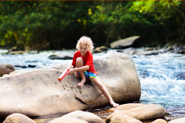 Children hiking in Alps mountains crossing river. Kids play in water at mountain in Austria. Spring family vacation. Little boy and girl on hike trail. Outdoor fun. Active recreation with children.