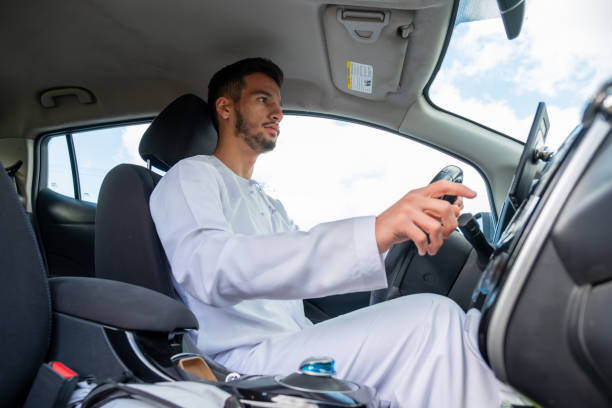 istock A cheerful young man with a beard, wearing a traditional Middle-Eastern outfit, smiles confidently while seated in his car. He appears to be enjoying a drive through a scenic countryside 2156868872