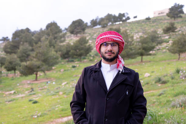 An Arab man in nature clears his mind and thinks positively about the future, surrounded by trees and clouds wearing a jacket due to change in climate