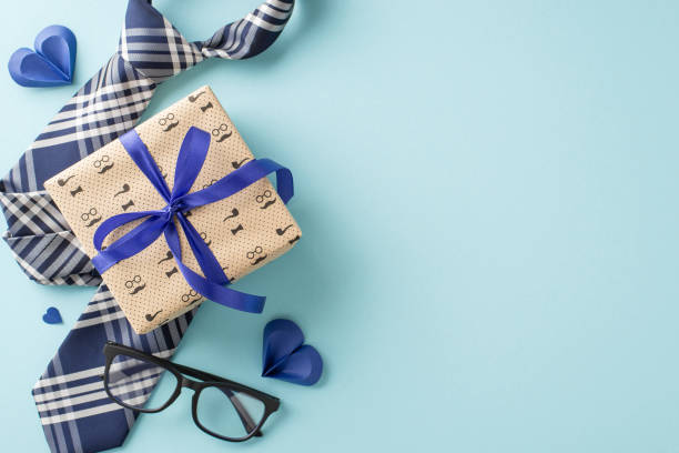istock A beautifully wrapped Fathers Day gift, complete with a stylish tie, glasses, and decorative hearts on a soft blue background 2156875214