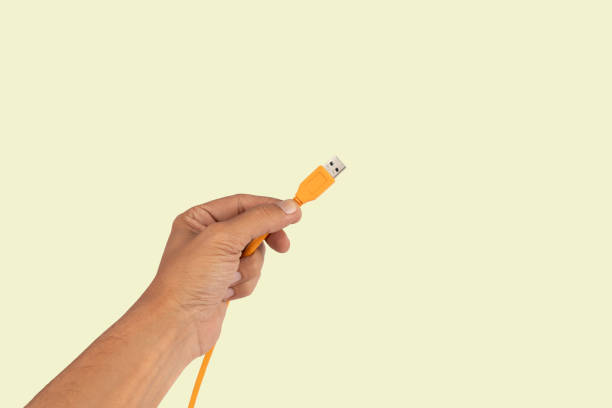 istock Black male hand holding an orange USB cable isolated on light green background 2156878016