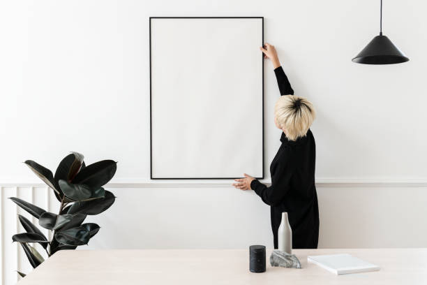 istock Blond haired Asian woman hanging a blank frame on a white wall 2156881371