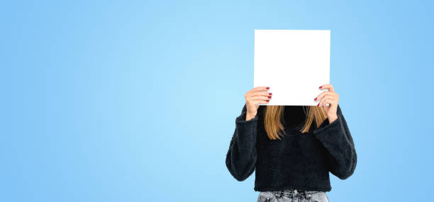 istock Young woman hiding face with blank mock up banner, empty colored background 2156881533