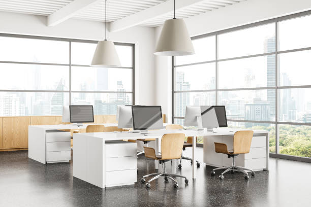 istock Stylish coworking interior with pc computers on desks in row, panoramic window 2156882127