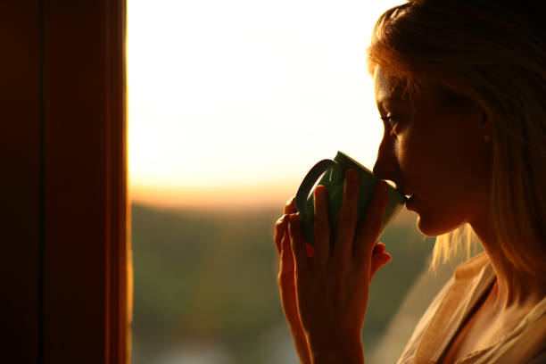 istock Thoughtful woman drinking coffee looking away through a window 2156883972