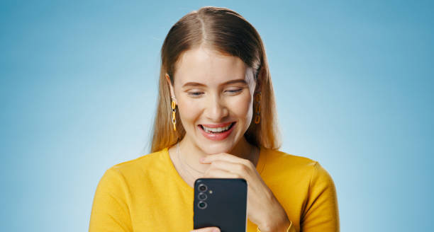 istock Woman, happy and reading with smartphone in studio, blog update and message notification on networking app. Social media, communication and smile for news or email, blue background and online survey 2156885716