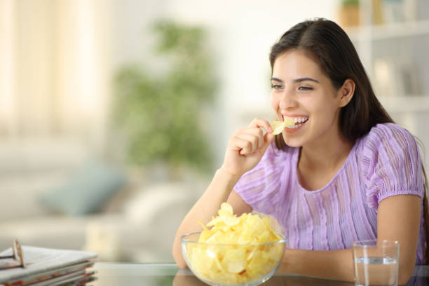 istock Woman laughing and eating potato chips alone at home 2156886439