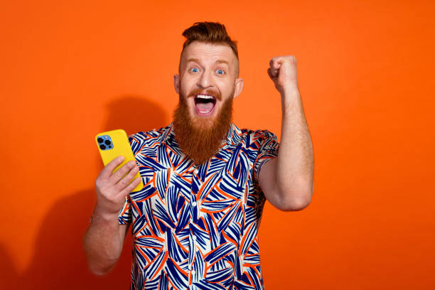 istock Photo of lucky excited guy dressed print shirt winking winning game modern device empty space isolated orange color background 2156895340