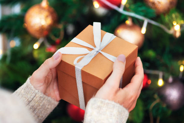 istock Woman holding a brown present near a Christmas tree 2156899155