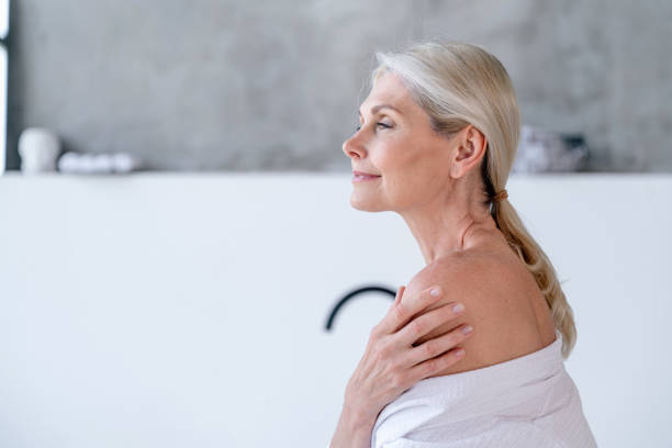 istock Mature woman in bathrobe standing in white bathroom with copy space on background 2156908079