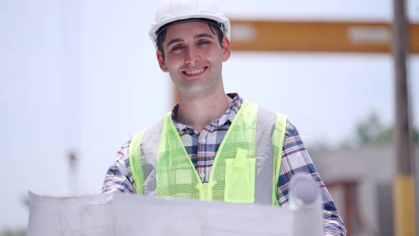 istock Engineer or building contractors or architect who have experience and expertise in building design and construction wearing safety uniform, standing hold blueprint in construction site, smiling proudly and looking at camera. 2156913506
