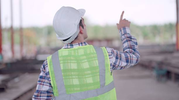 istock Rear view. Engineer or contractors or architect wearing safety vest and haedhat working in construction site, building or housing project, check the construction progrss of the building or quality of the product in production line at factory. 2156913578