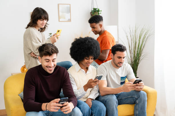 istock Four friends casually scroll through their smartphones while sitting on a yellow couch 2156915464