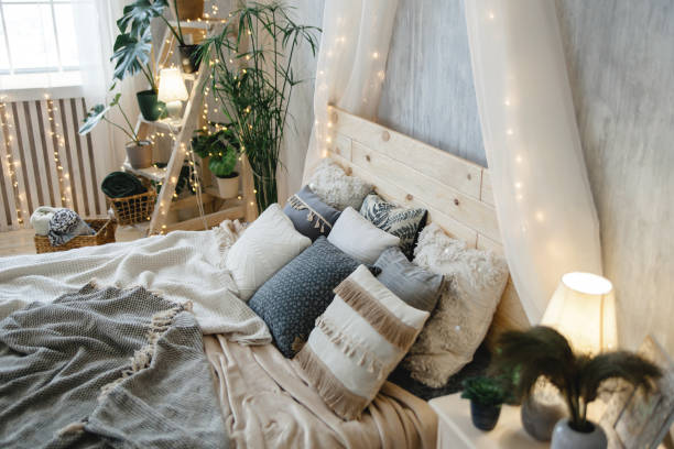istock Boho bed featuring wooden headboard, assorted pillows, soft blankets, light grey walls, houseplants, and fairy lights. Room exudes warmth and tranquility with a stylish touch 2156917314