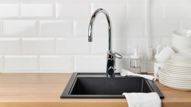 Banner with clean washed white tableware near black kitchen sink with a chrome faucet on wooden counter, and white subway tile backsplash with dishwashing liquid and brush