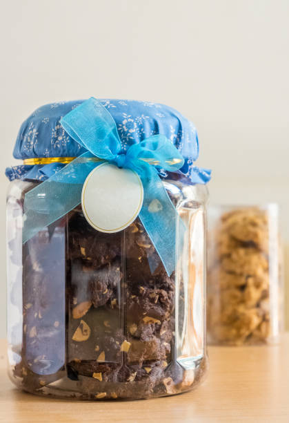Full jar of delicious cookies with chocolate chips on a white table, with copy space for text.  Tasty chocolate chip cookies in a clear glass jar, on a light kitchen table.