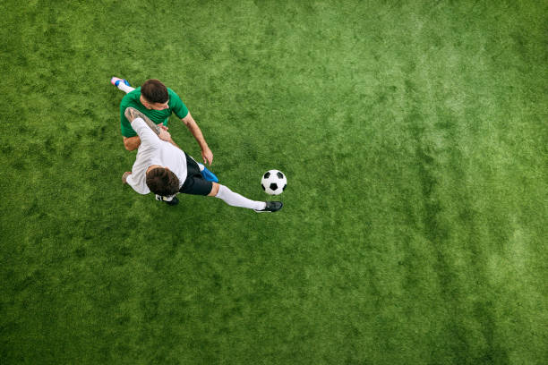 istock Aerial view. Player in white uniform kicks ball, while opponent in green gets ready to block on green lush playground. 2156924198