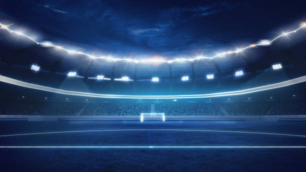 istock Under dazzling stadium lights, empty football field ready for intense match and shouting crowd of fans on background. 2156925649