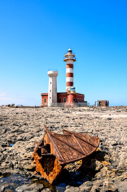 istock A rusty anchor is sitting on the ground next to a lighthouse 2156930642
