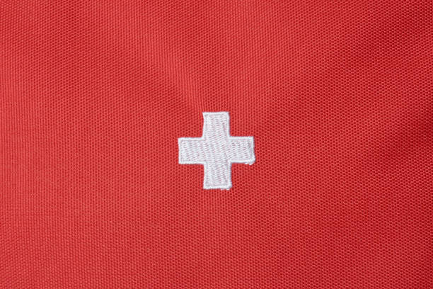 white hospital plus or medical cross sign on red textured fabric surface background, embroidered swiss national flag with copy space
