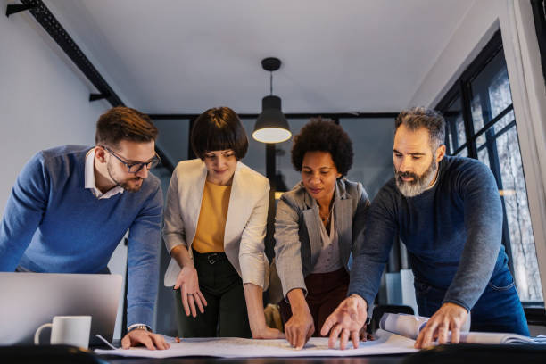 istock Focused interracial architects pointing at blueprints on a table on a meeting at boardroom. 2156938148