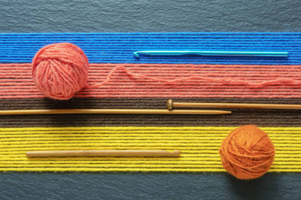 Hobbies and knitting concept, background. Rows of woolen threads,  knitting needles, crochet hooks and balls on wool on black table. Copy space