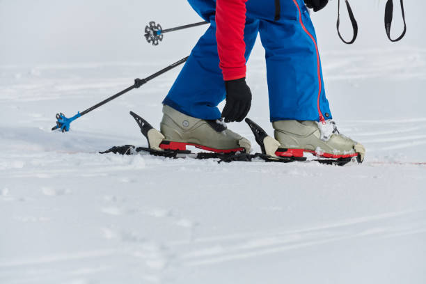 Close-up on the boots and bindings of a skier about to set off down a piste, with snowcapped mountains in the background.