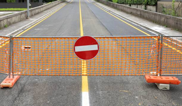 istock No entry traffic sign on temporary safety orange plastic netting fence, with a closed  empty two lane road  behind it. 2156952814