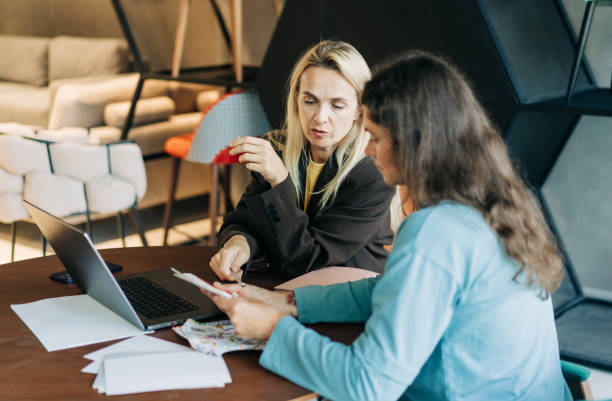 istock A female consultant works in a show room with a client using a laptop and a catalog. 2156956842