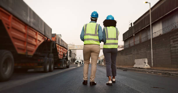 istock Construction worker, team and walking with discussion at logistics site in morning for vehicle inspection or cargo export. Shipping industry, inspectors and outdoor with back for quality assurance 2156970881