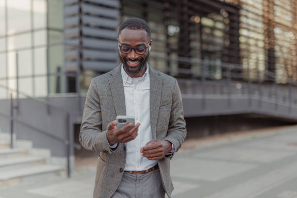 istock Modern Smiling African-American Businessman Having a Phone Call While Walks Outside Office Building 2156974941