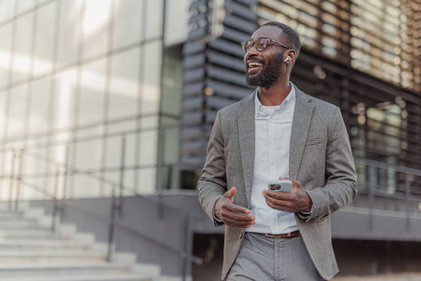 istock Modern Smiling African-American Businessman Having a Phone Call While Walks Outside Office Building 2156975259