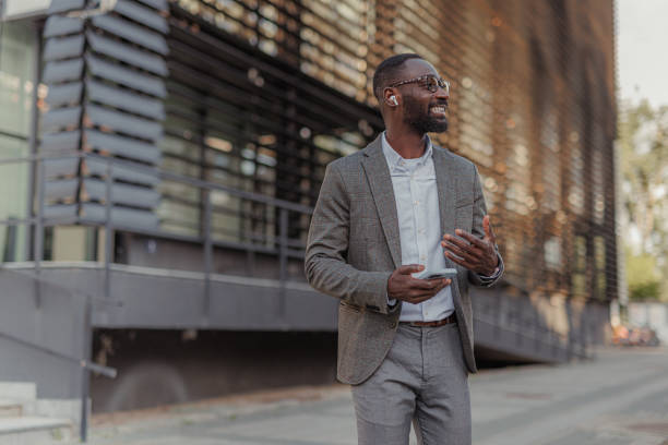 istock Modern Smiling African-American Businessman Having a Phone Call While Walks Outside Office Building 2156975372