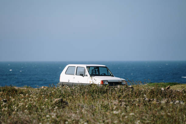 A small, old car parked by the sea