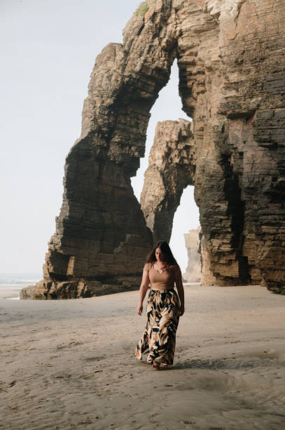 istock Woman walking on a beach with natural rock arches 2156980174