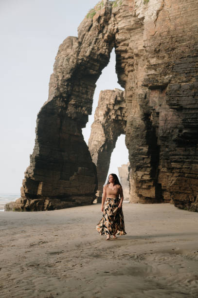 istock Woman walking on a beach with natural rock arches 2156980182