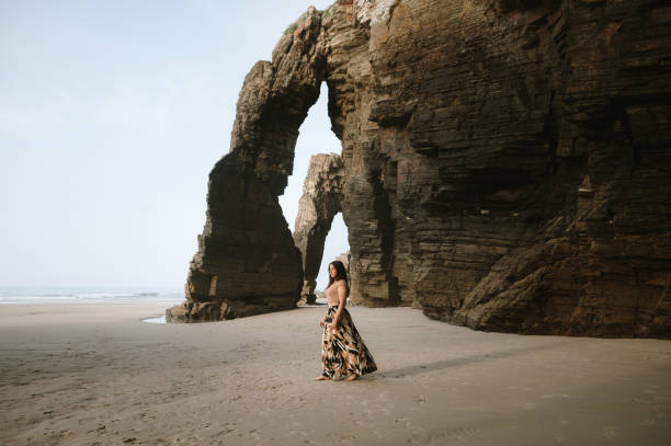 istock Woman walking on a beach with natural rock arches 2156980452