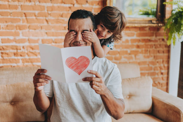 istock Smiling child hiding father's eyes and handing gift postcard 2156983773